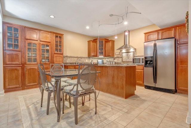 kitchen featuring light stone counters, a center island, appliances with stainless steel finishes, decorative backsplash, and wall chimney range hood