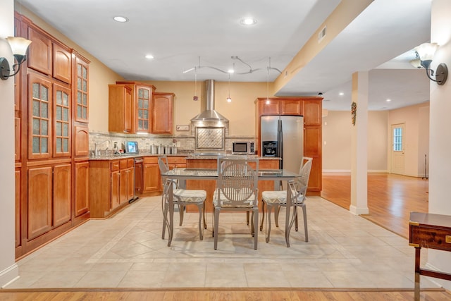 kitchen with wall chimney exhaust hood, a breakfast bar area, tasteful backsplash, a kitchen island, and stainless steel appliances