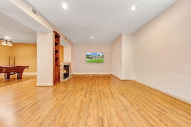 unfurnished living room with a tiled fireplace, built in features, light wood-type flooring, and billiards