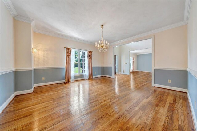 spare room with crown molding, a notable chandelier, and light wood-type flooring