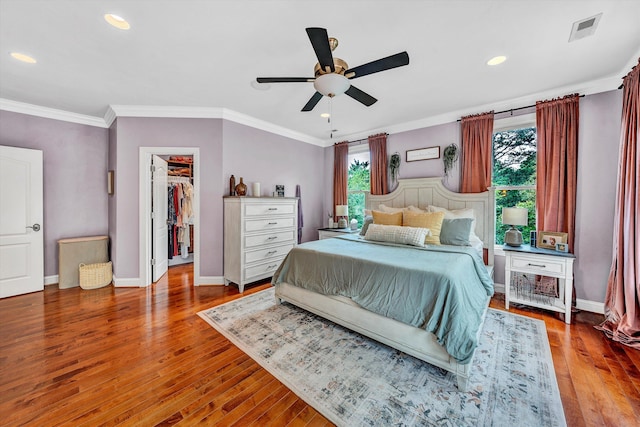 bedroom with crown molding, hardwood / wood-style floors, ceiling fan, a spacious closet, and a closet