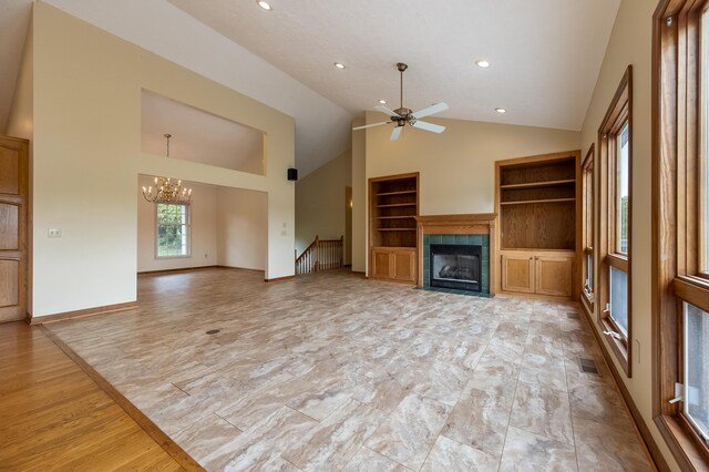 unfurnished living room featuring high vaulted ceiling, built in shelves, light wood-type flooring, ceiling fan with notable chandelier, and a tiled fireplace