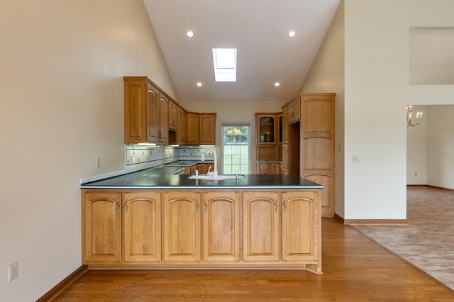 kitchen featuring backsplash, a skylight, light wood-type flooring, high vaulted ceiling, and kitchen peninsula