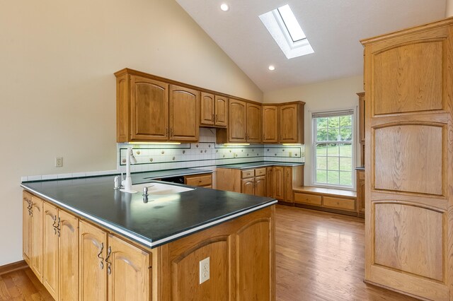 kitchen with kitchen peninsula, light hardwood / wood-style floors, decorative backsplash, and a skylight