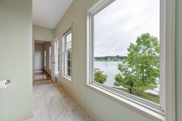 corridor with a wealth of natural light, light tile patterned flooring, and a water view