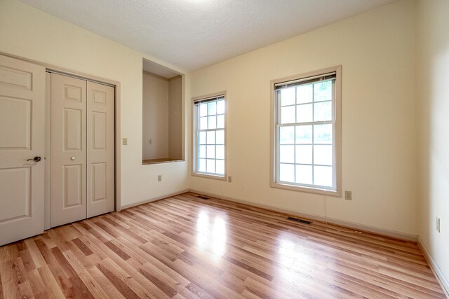 unfurnished bedroom with light wood-type flooring, a closet, and a textured ceiling