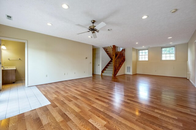 unfurnished living room featuring ceiling fan, light hardwood / wood-style floors, and a textured ceiling