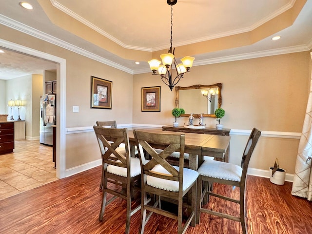 dining room with a notable chandelier, light hardwood / wood-style floors, a raised ceiling, and crown molding