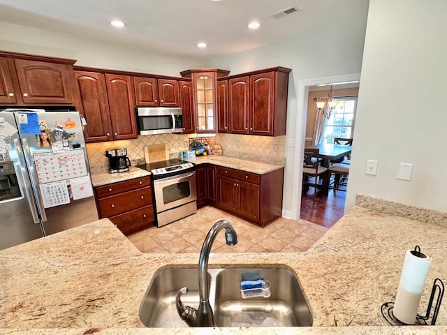 kitchen with sink, stainless steel appliances, light hardwood / wood-style flooring, and light stone countertops