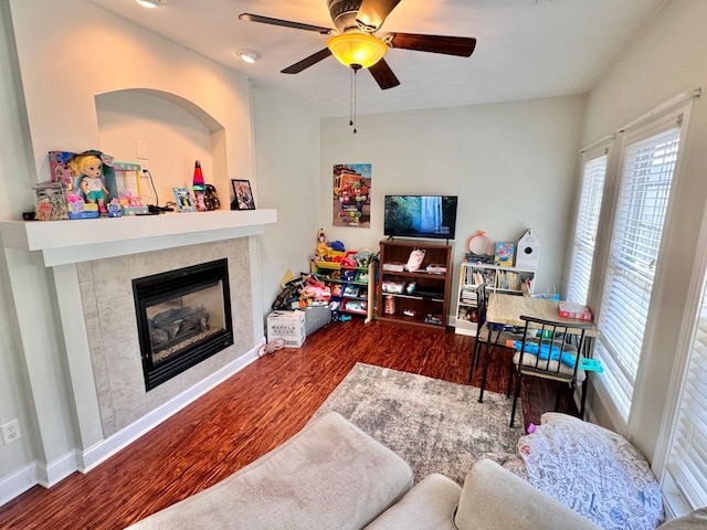 living room featuring ceiling fan, a wealth of natural light, a tile fireplace, and dark hardwood / wood-style flooring