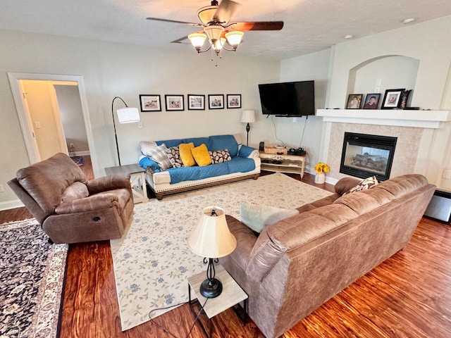 living room featuring ceiling fan, a tiled fireplace, and wood-type flooring