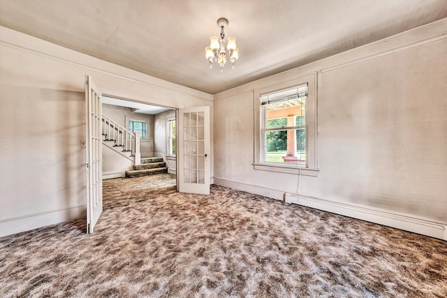 carpeted empty room featuring a chandelier, baseboard heating, and french doors