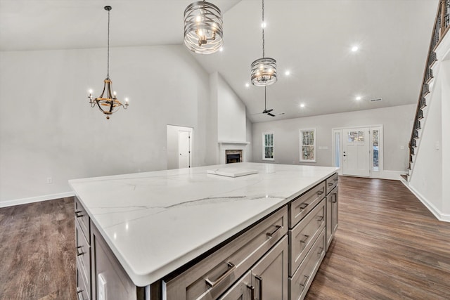 kitchen with ceiling fan with notable chandelier, a center island, dark wood-type flooring, and hanging light fixtures