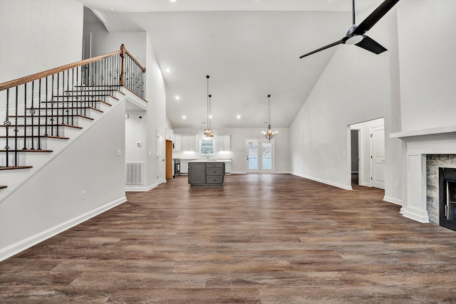 unfurnished living room featuring ceiling fan with notable chandelier, dark hardwood / wood-style flooring, high vaulted ceiling, and a tiled fireplace