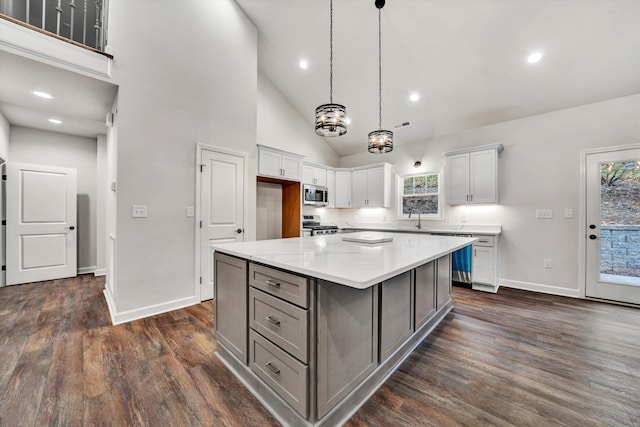 kitchen with appliances with stainless steel finishes, dark hardwood / wood-style flooring, high vaulted ceiling, white cabinets, and a kitchen island