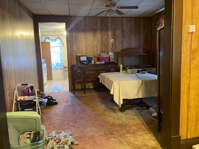 bedroom featuring ceiling fan, wood walls, carpet flooring, and a drop ceiling