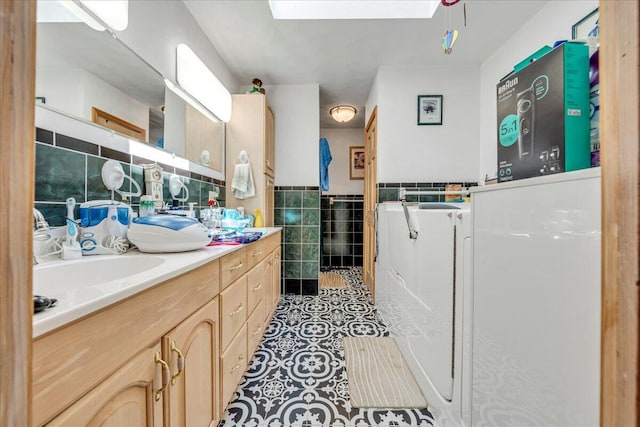 bathroom with tile patterned flooring, double vanity, wainscoting, a skylight, and tile walls