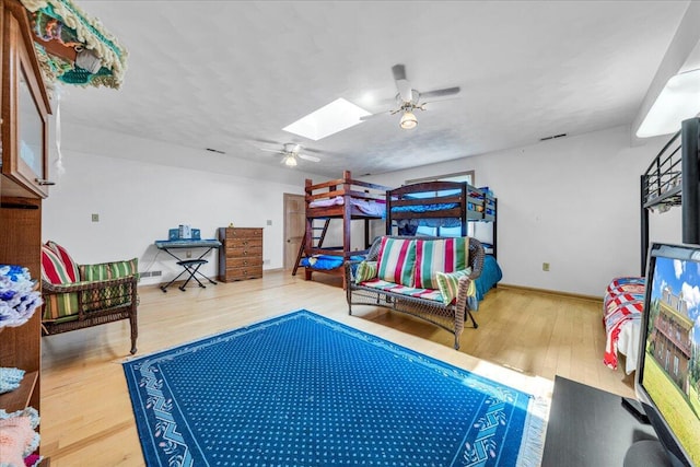 bedroom featuring visible vents, a ceiling fan, wood finished floors, a skylight, and baseboards