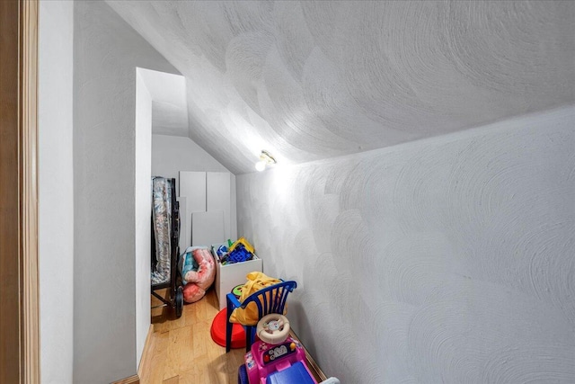 recreation room featuring a textured ceiling, lofted ceiling, and wood finished floors