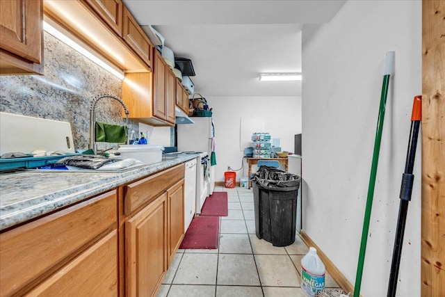 kitchen with light tile patterned floors, baseboards, brown cabinets, and under cabinet range hood