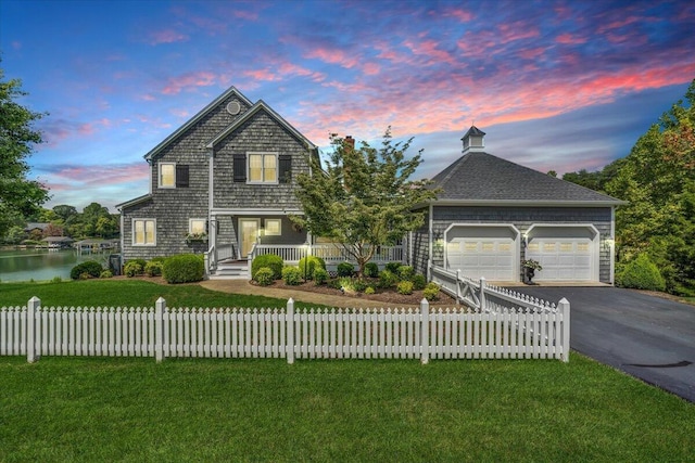 front facade with covered porch, a garage, a water view, and a lawn