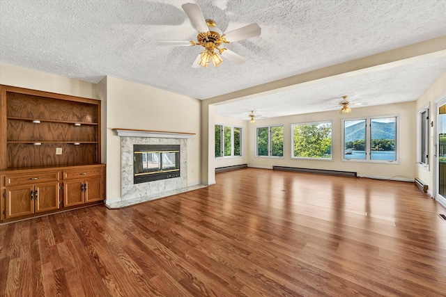 unfurnished living room with a textured ceiling, baseboard heating, a fireplace, and wood finished floors