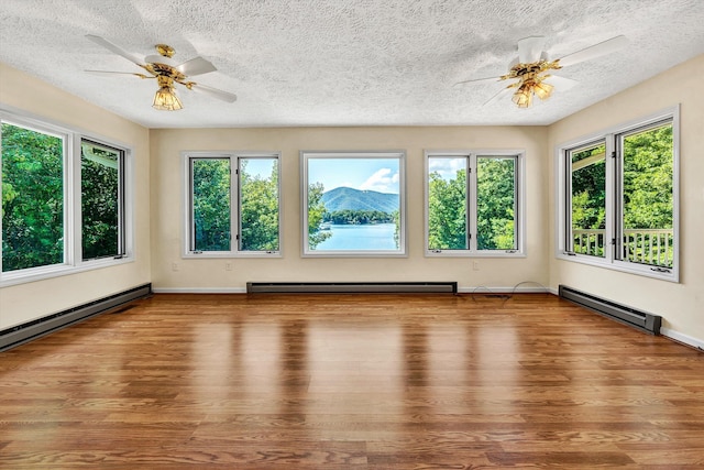 unfurnished sunroom with a ceiling fan, a baseboard radiator, and a wealth of natural light