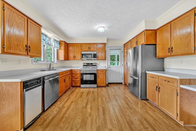 kitchen featuring ornamental molding, a textured ceiling, light hardwood / wood-style flooring, stainless steel appliances, and sink