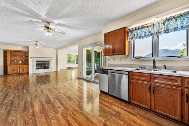 kitchen with dishwasher, a premium fireplace, wood finished floors, light countertops, and a sink