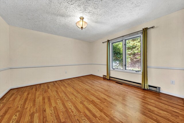 unfurnished room featuring a textured ceiling, baseboard heating, and hardwood / wood-style floors