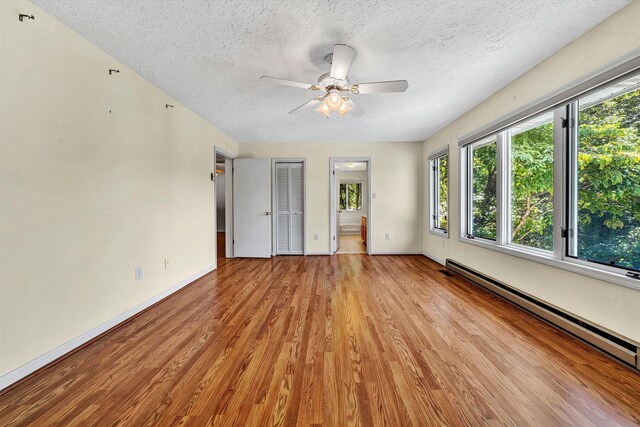 spare room featuring light wood-type flooring, ceiling fan, baseboard heating, and a textured ceiling