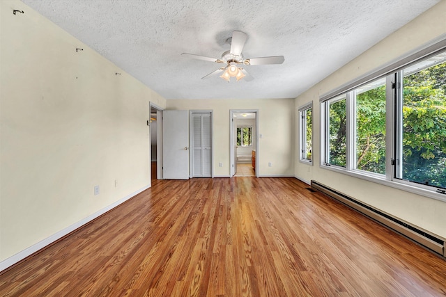 unfurnished bedroom featuring a textured ceiling, baseboards, baseboard heating, and wood finished floors