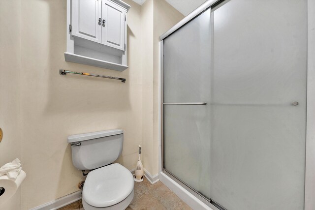 bathroom with a shower with shower door, toilet, and tile patterned floors