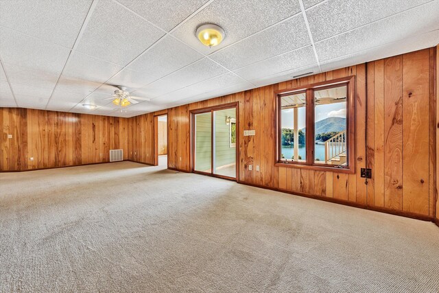 carpeted spare room with a mountain view, wood walls, a paneled ceiling, and ceiling fan