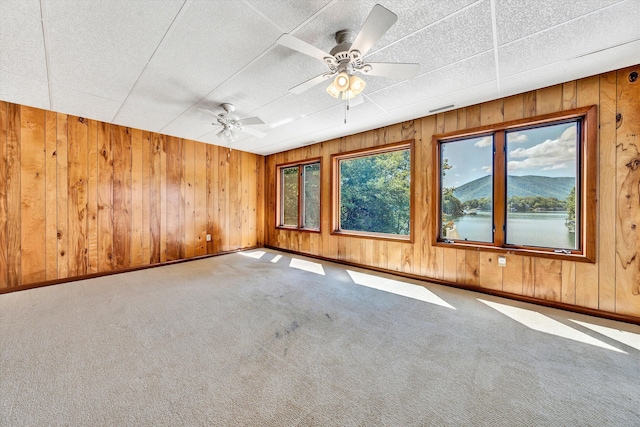 empty room with a mountain view, wooden walls, ceiling fan, and carpet