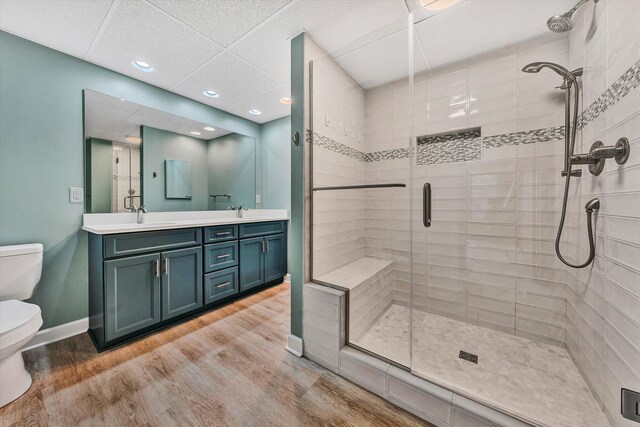 bathroom with a shower with door, vanity, hardwood / wood-style floors, toilet, and a drop ceiling