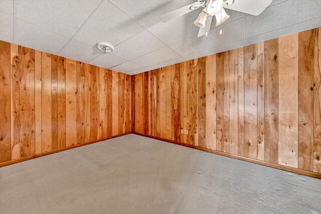 carpeted spare room featuring ceiling fan, a paneled ceiling, and wooden walls