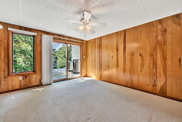 carpeted spare room featuring a ceiling fan, wooden walls, and baseboards