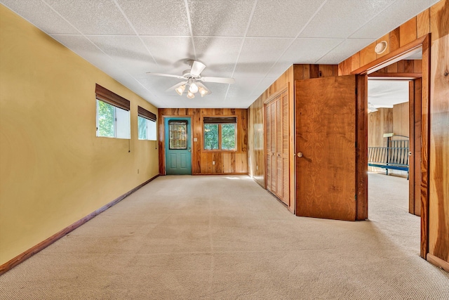 unfurnished room with ceiling fan, wood walls, carpet flooring, and baseboards