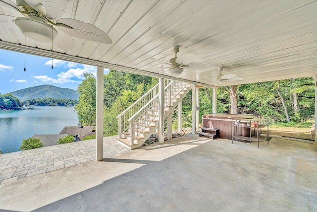 view of patio with ceiling fan, a water and mountain view, and a hot tub