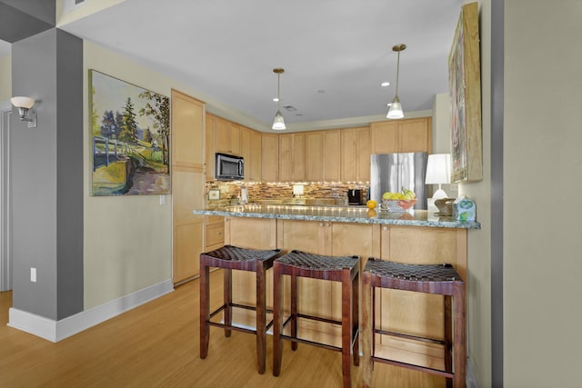 kitchen with appliances with stainless steel finishes, light stone countertops, light brown cabinetry, and light hardwood / wood-style flooring