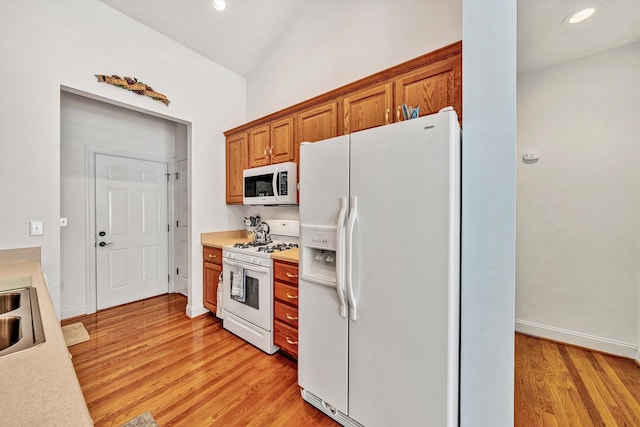 kitchen with light hardwood / wood-style flooring, white appliances, and vaulted ceiling