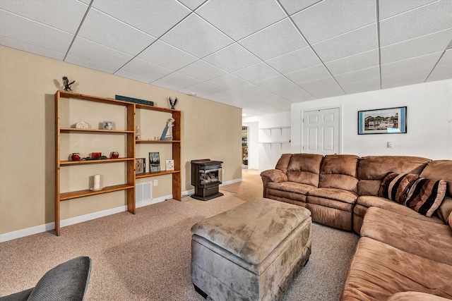 carpeted living room with a paneled ceiling and a wood stove