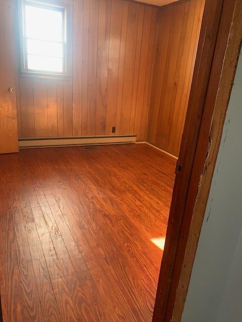 unfurnished room with baseboard heating, hardwood / wood-style floors, and wood walls