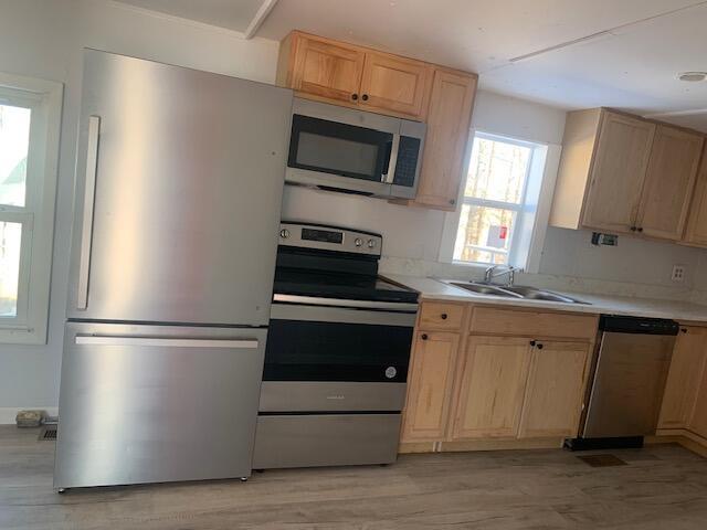 kitchen featuring stainless steel appliances, sink, light brown cabinetry, and light wood-type flooring