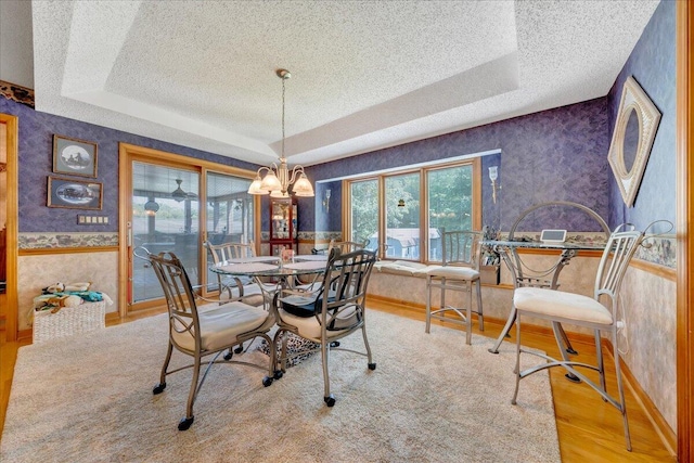 dining space with a notable chandelier, a tray ceiling, light hardwood / wood-style flooring, and a textured ceiling