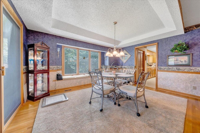 dining area with a notable chandelier, light hardwood / wood-style flooring, a raised ceiling, and a textured ceiling