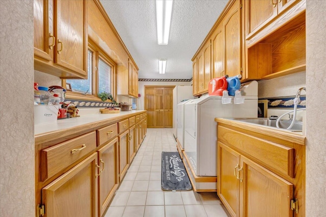 laundry room featuring light tile patterned floors, sink, washing machine and dryer, cabinets, and a textured ceiling