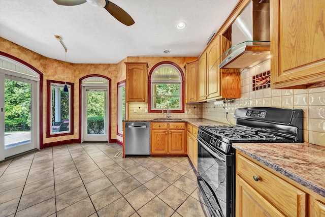 kitchen featuring wall chimney exhaust hood, stainless steel dishwasher, ceiling fan, light stone counters, and black gas range