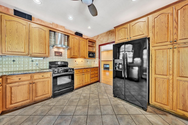 kitchen featuring black appliances, dark stone countertops, light tile patterned floors, ceiling fan, and wall chimney range hood